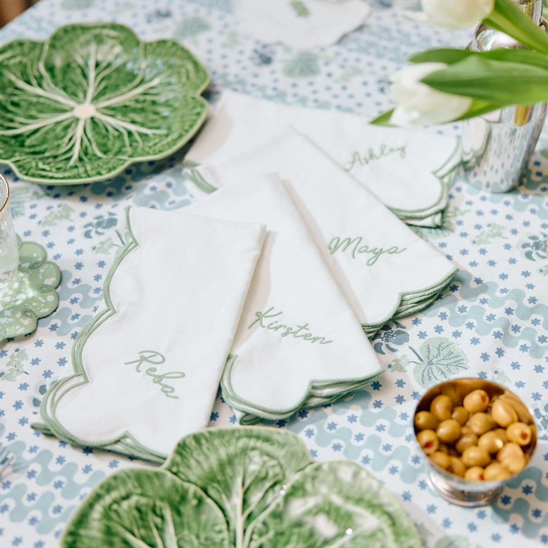 White Weezie scallop dinner napkins with green embroidered edges and names, set on a table with green cabbage plates