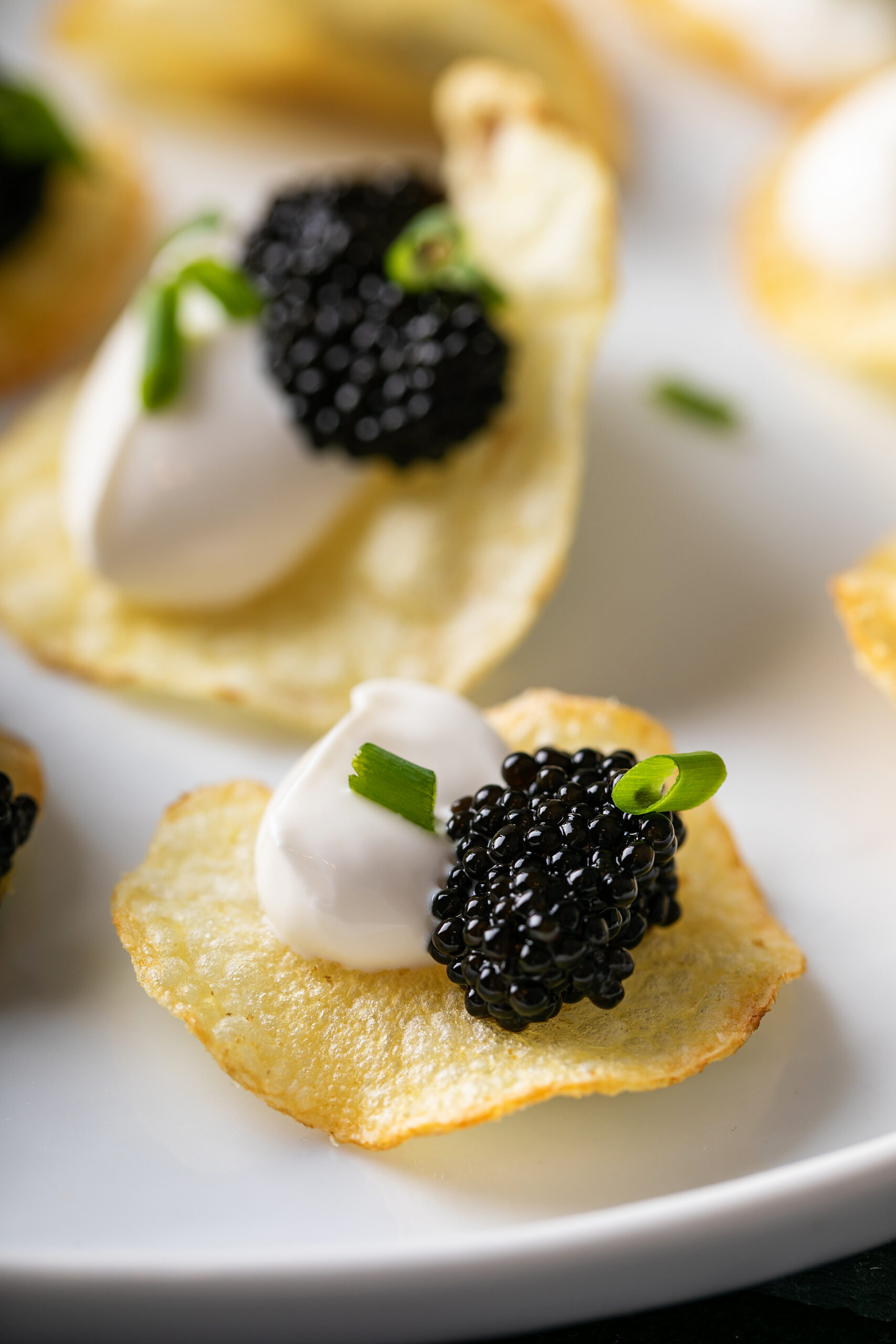 Close-up of a potato chip topped with crème fraîche, caviar and chives