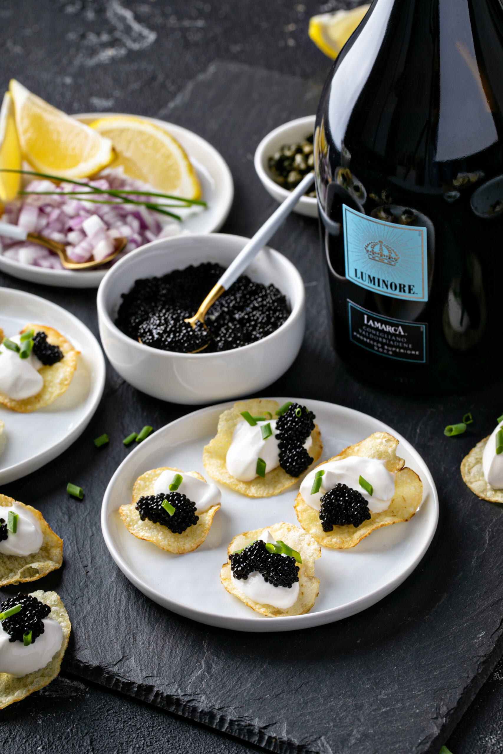 Bottle of La Marca Luminore prosecco beside a bowl of caviar and a plate of caviar potato chips