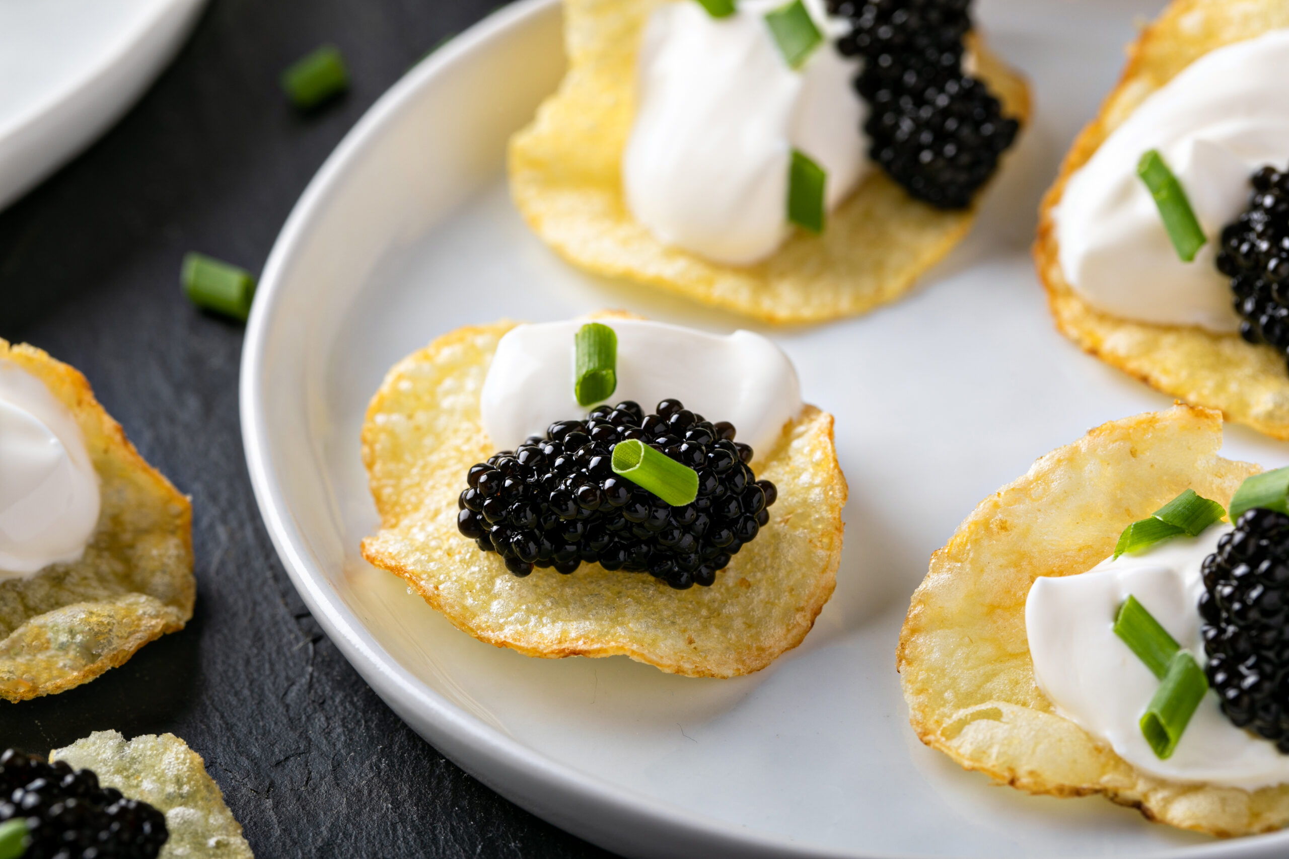 Close-up of caviar potato chips with crème fraîche and chives on a white plate