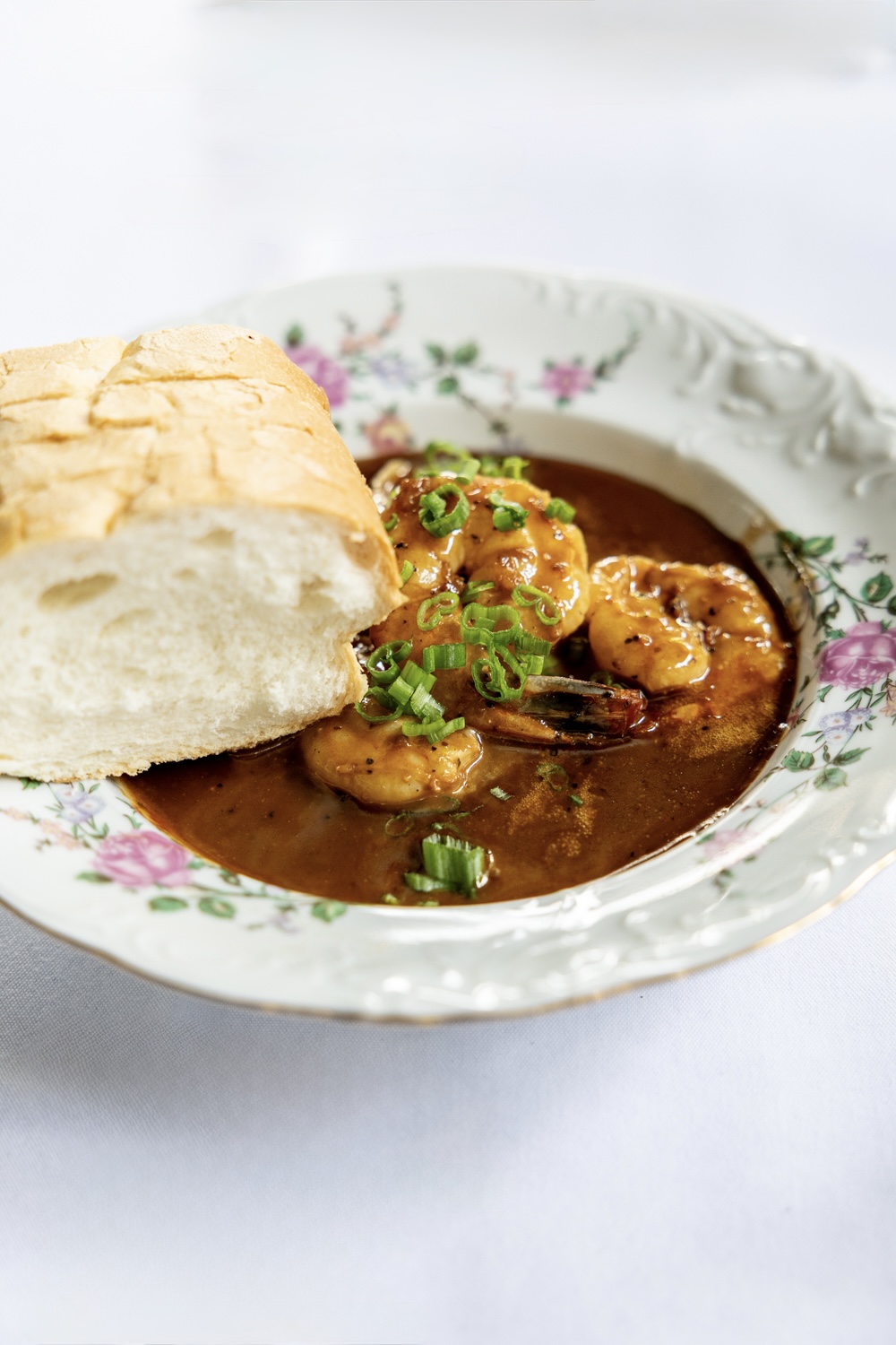 Shrimp in a rich, dark sauce with crusty bread in a floral china bowl at Miscellanea Spirit House