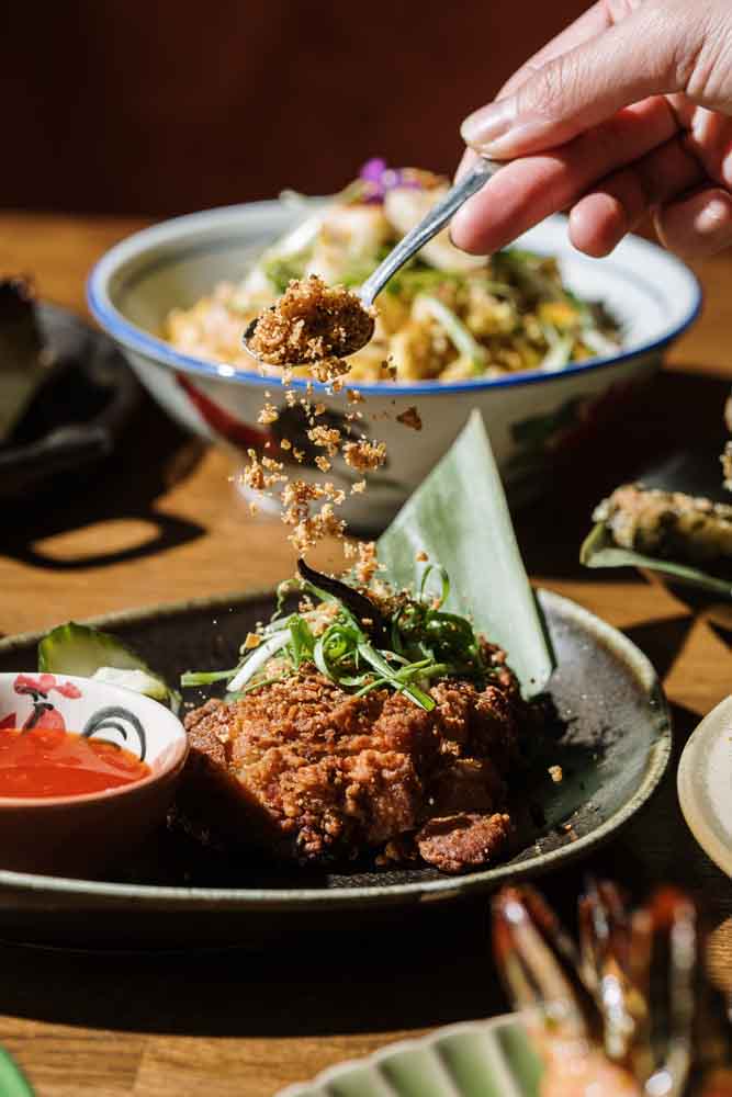 A diner lifting noodles from a bowl beside crispy fried chicken at Tipsy Thaiger in Roswell