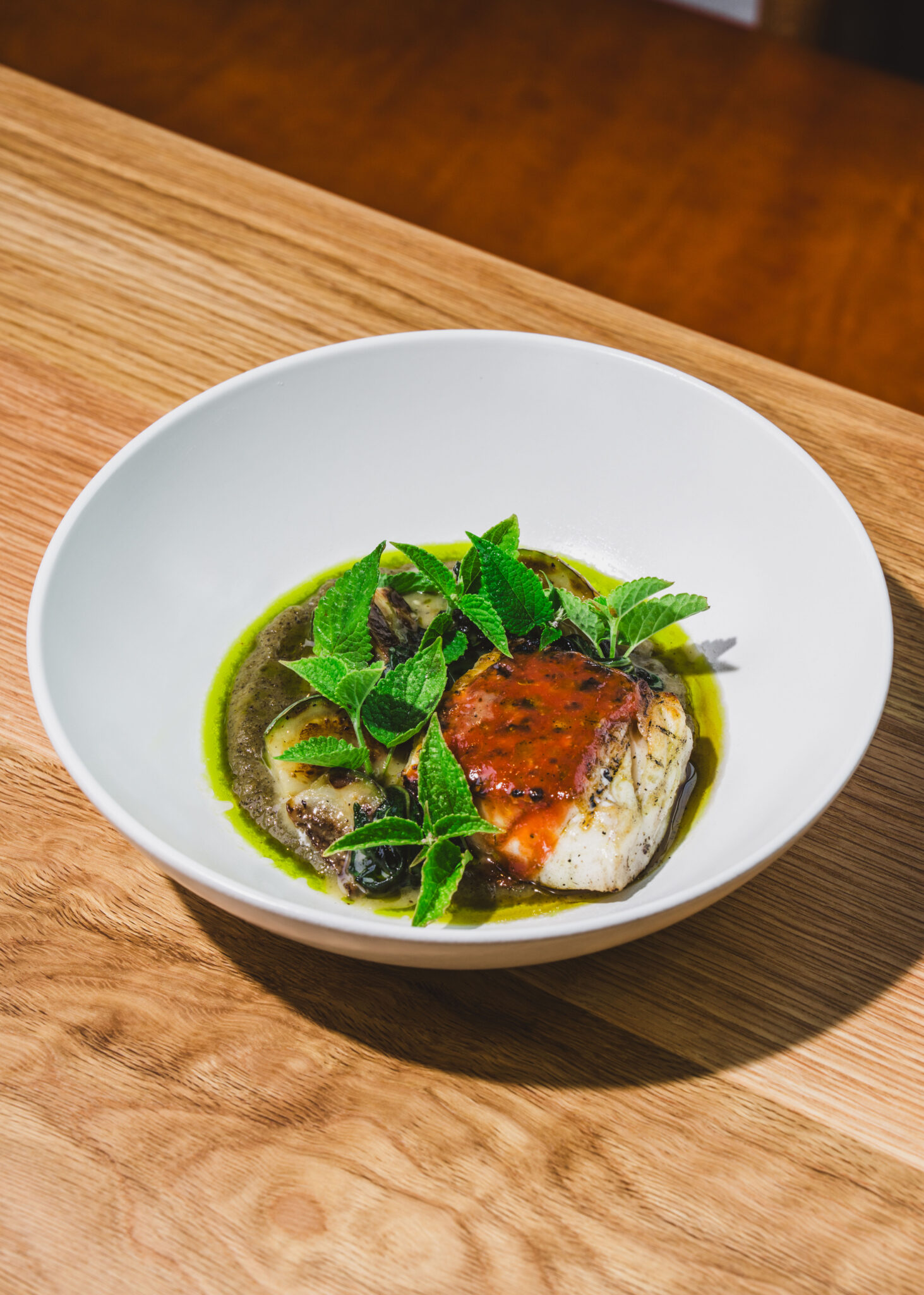 A composed dish with fresh greens and a bright orange sauce in a white bowl on a wooden table at So. Fox in Atlanta