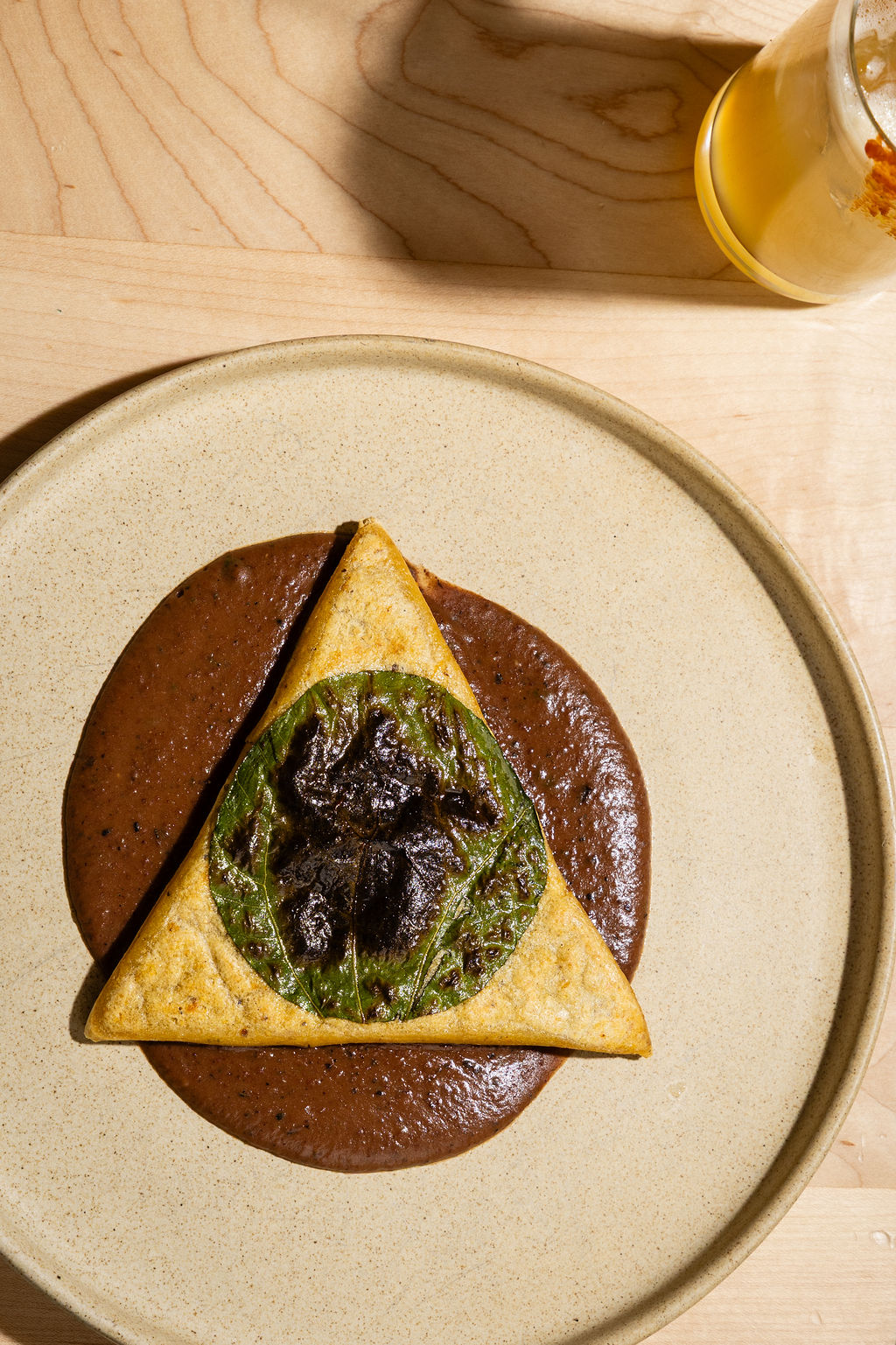 A triangular masa dish over dark mole on a cream plate at Maiz De La Vida in Nashville