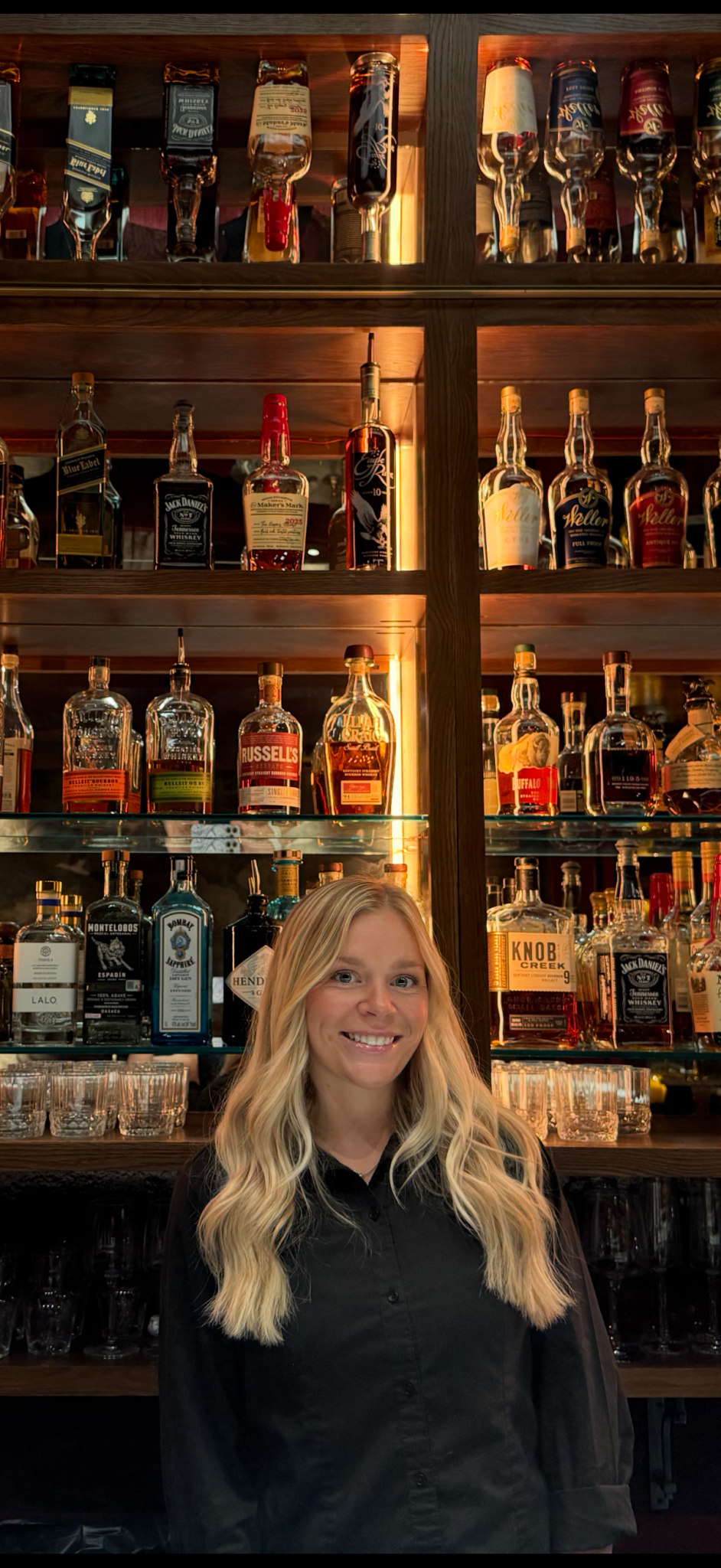 Ally Bowen, winner of the MICHELIN Exceptional Cocktails Award, standing in front of the back bar at Miscellanea Spirit House