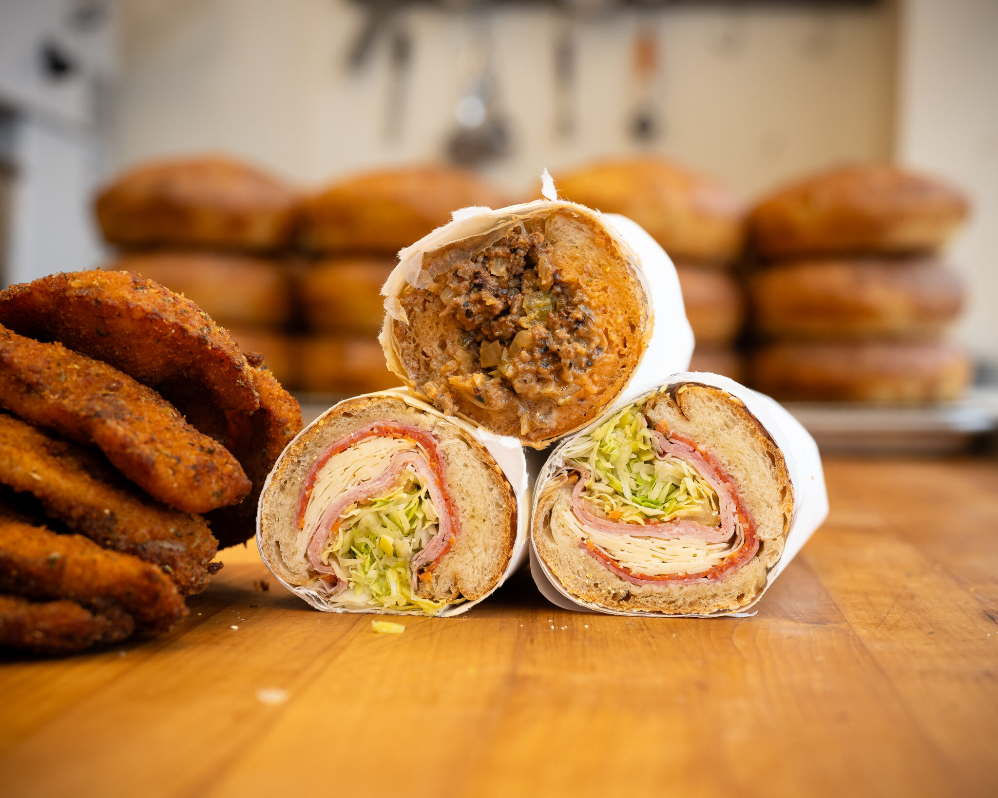 Stacked sandwiches beside fresh bread rolls at Ideal’s in Durham, North Carolina