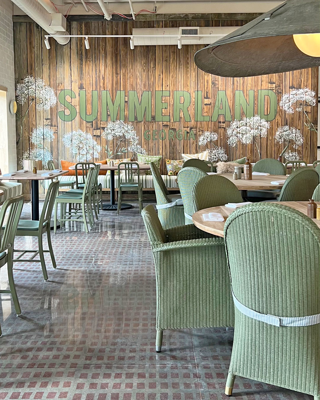 The sage green dining room at Summerland in Atlanta with woven chairs and a floral mural