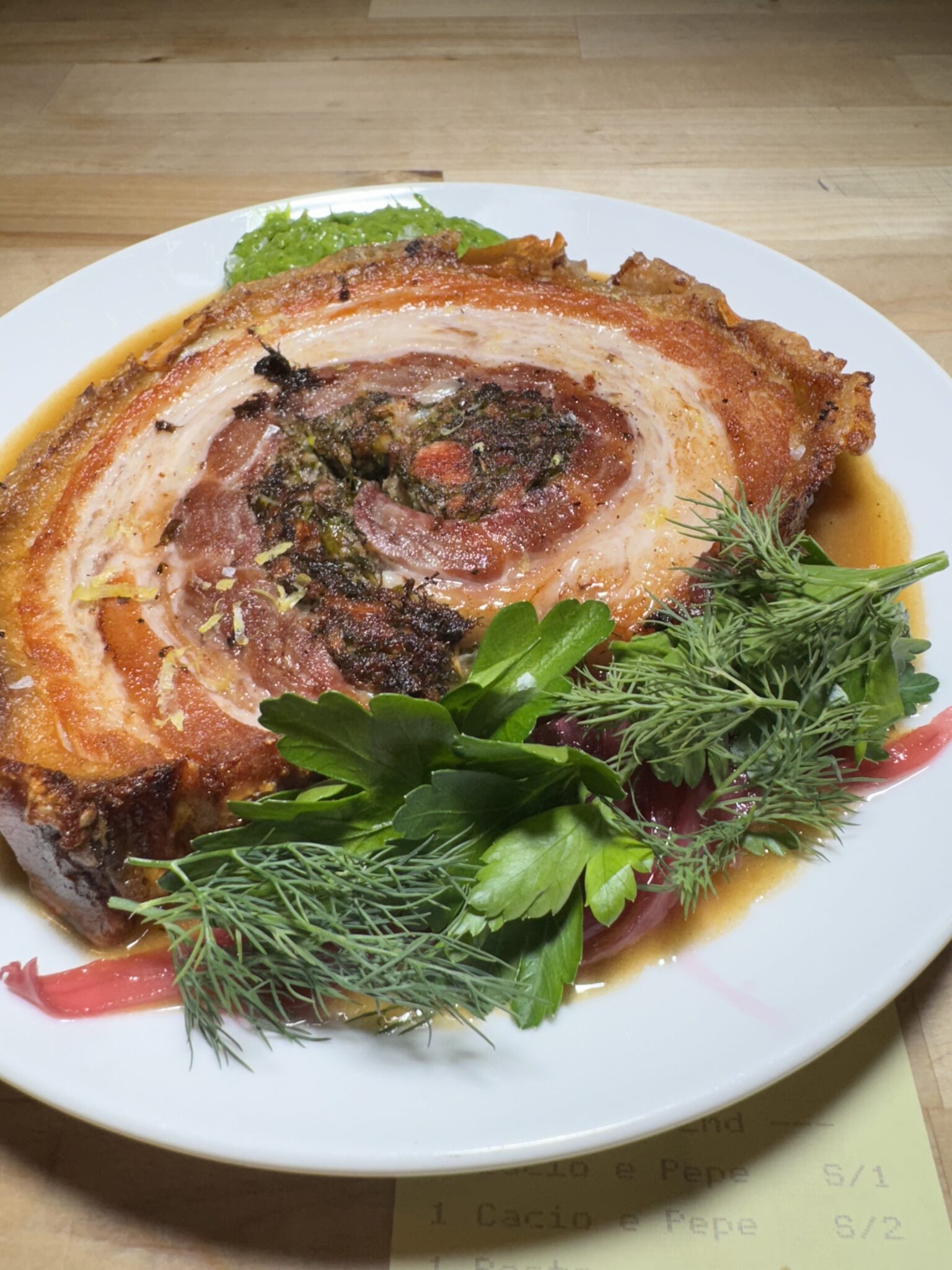 Sliced porchetta with fresh herbs on a white plate at Tesoro in Carrboro, North Carolina