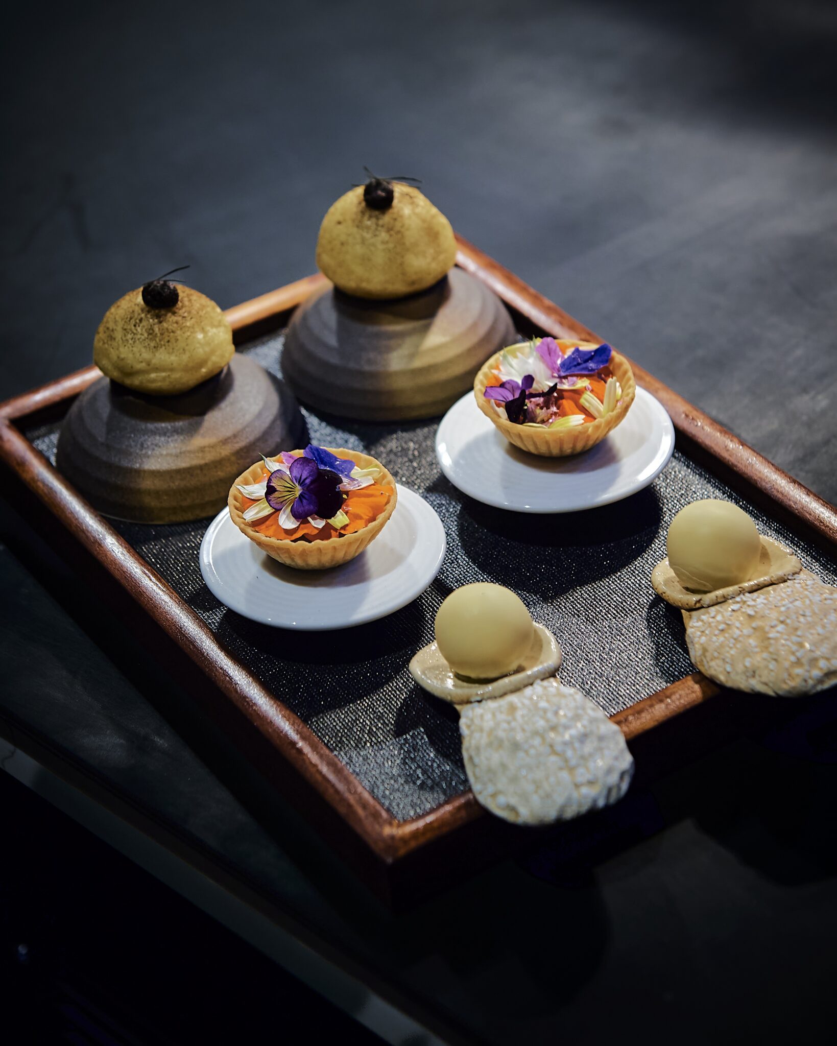 Small bites on stone pedestals arranged on a dark tray at Uberto Restaurant in Gay, Georgia