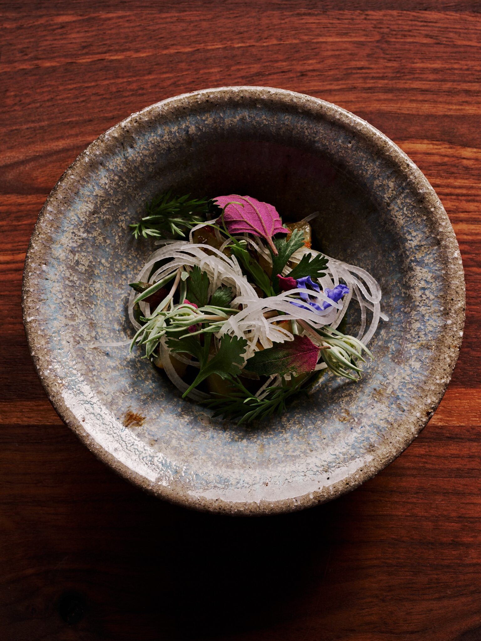 A layered vegetable course with edible flowers in a stoneware bowl at Uberto Restaurant