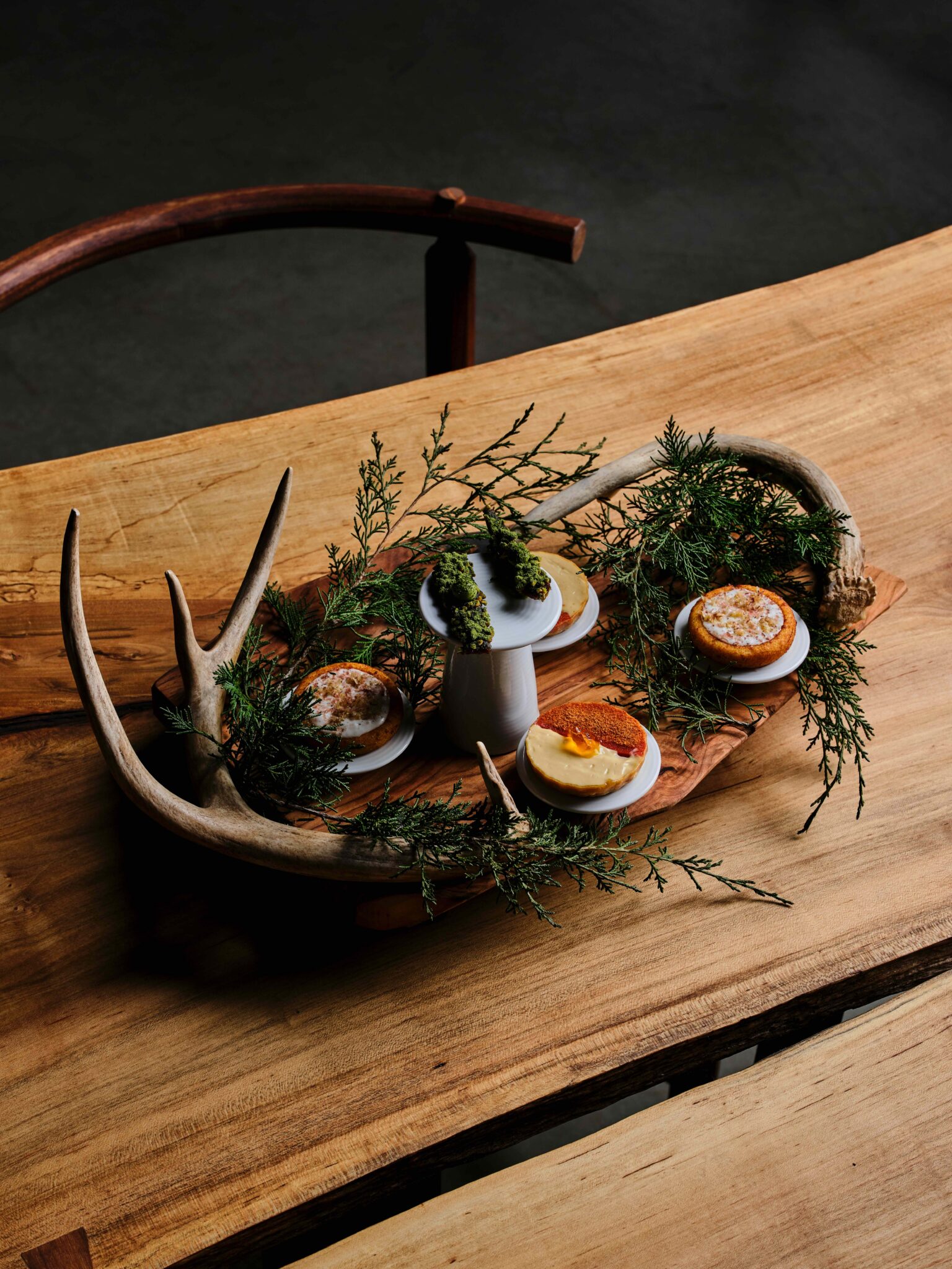 A seafood course garnished with herbs and antler on a live-edge wood board at Uberto Restaurant
