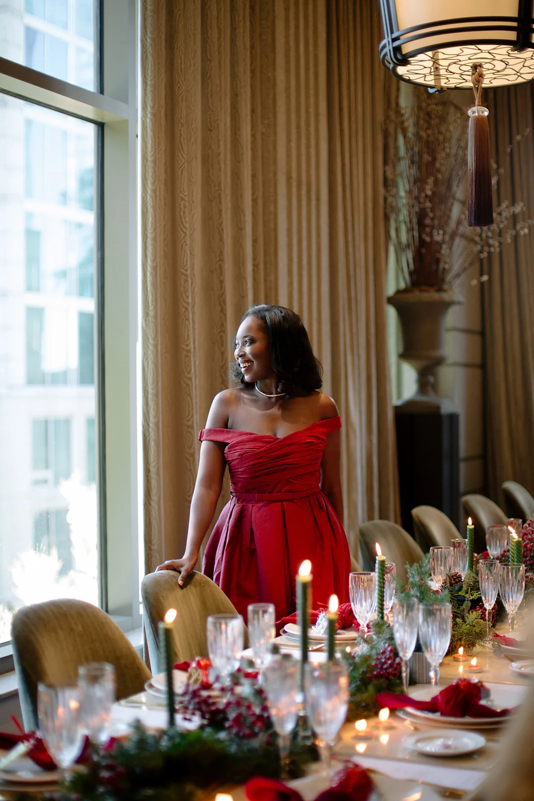 Erica A. Thomas in a red dress beside a candlelit holiday dinner table set for guests