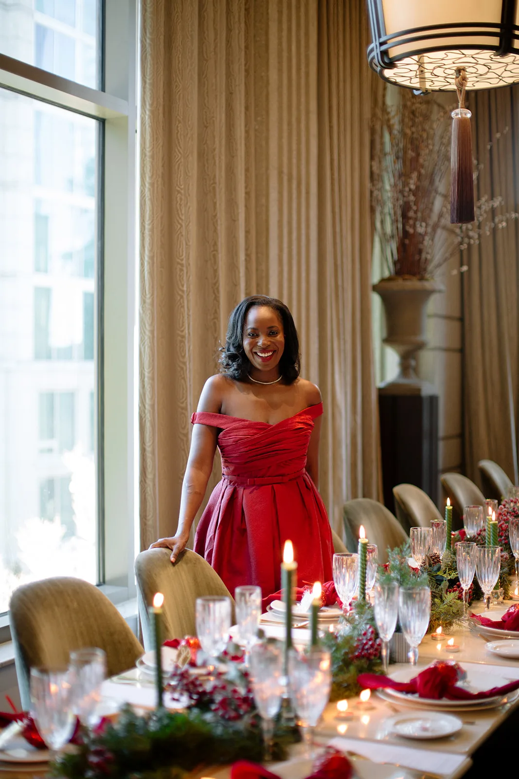 Erica A. Thomas smiling in a red off-the-shoulder dress beside her candlelit holiday dinner table