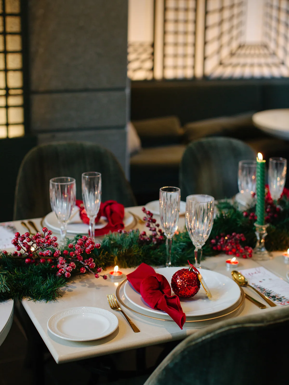 Holiday place setting with a red velvet napkin, red glitter ornament, gold flatware and a gold-rimmed charger beside a berry garland