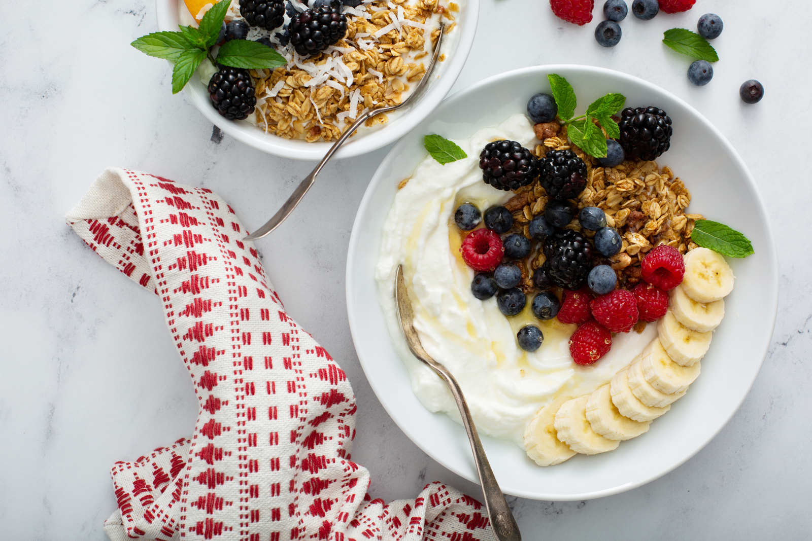 Greek yogurt bowl topped with berries, granola and sliced banana beside a red and white napkin